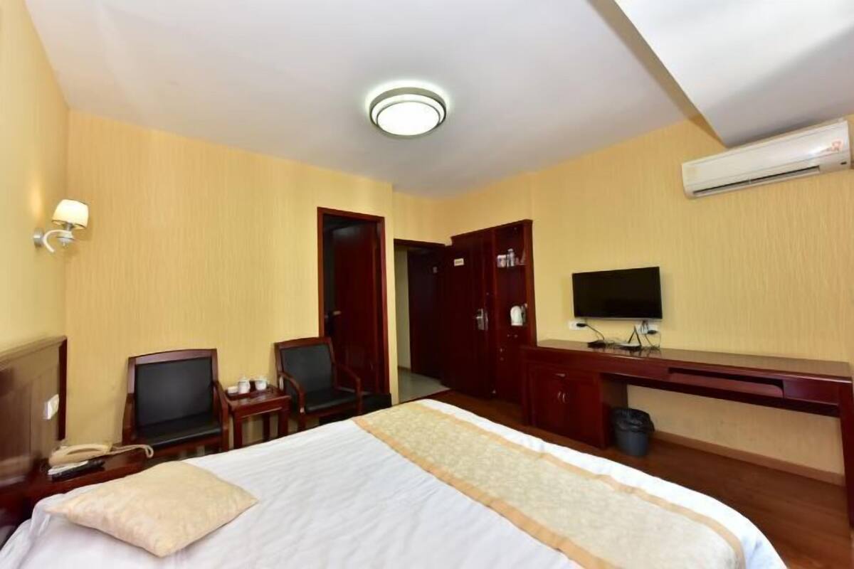 Una habitación de hotel con cama, escritorio, silla, televisor y aire acondicionado.