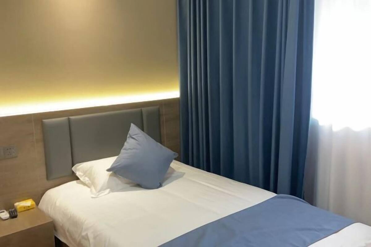 Una habitación de hotel con cama, mesita de noche y ventana con cortinas.