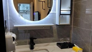 A modern bathroom with a large mirror, a white sink, a black faucet, and a towel dispenser. - XINYUN BUSINESS HOTEL (Zhoushan)