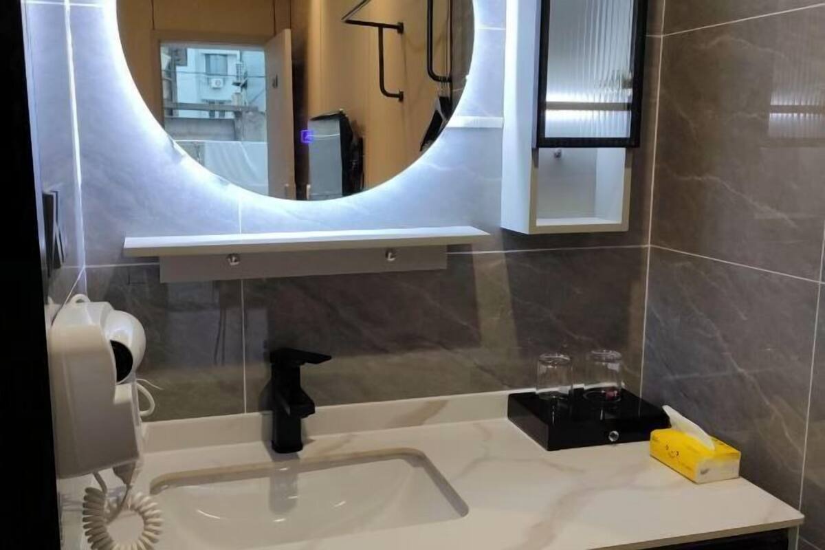Un baño moderno con un espejo grande, un lavamanos blanco, un grifo negro y un dispensador de toallas.