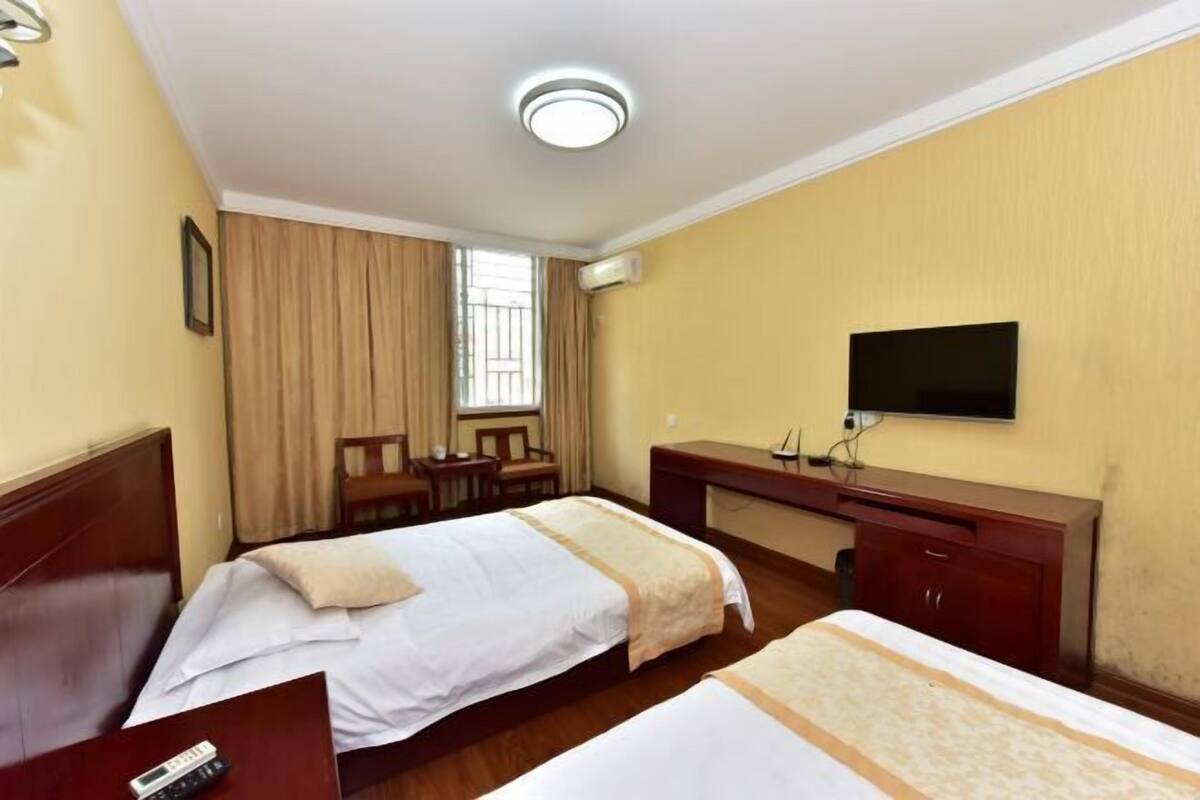 Habitación de hotel con dos camas, un escritorio, una silla, un televisor y un aire acondicionado.