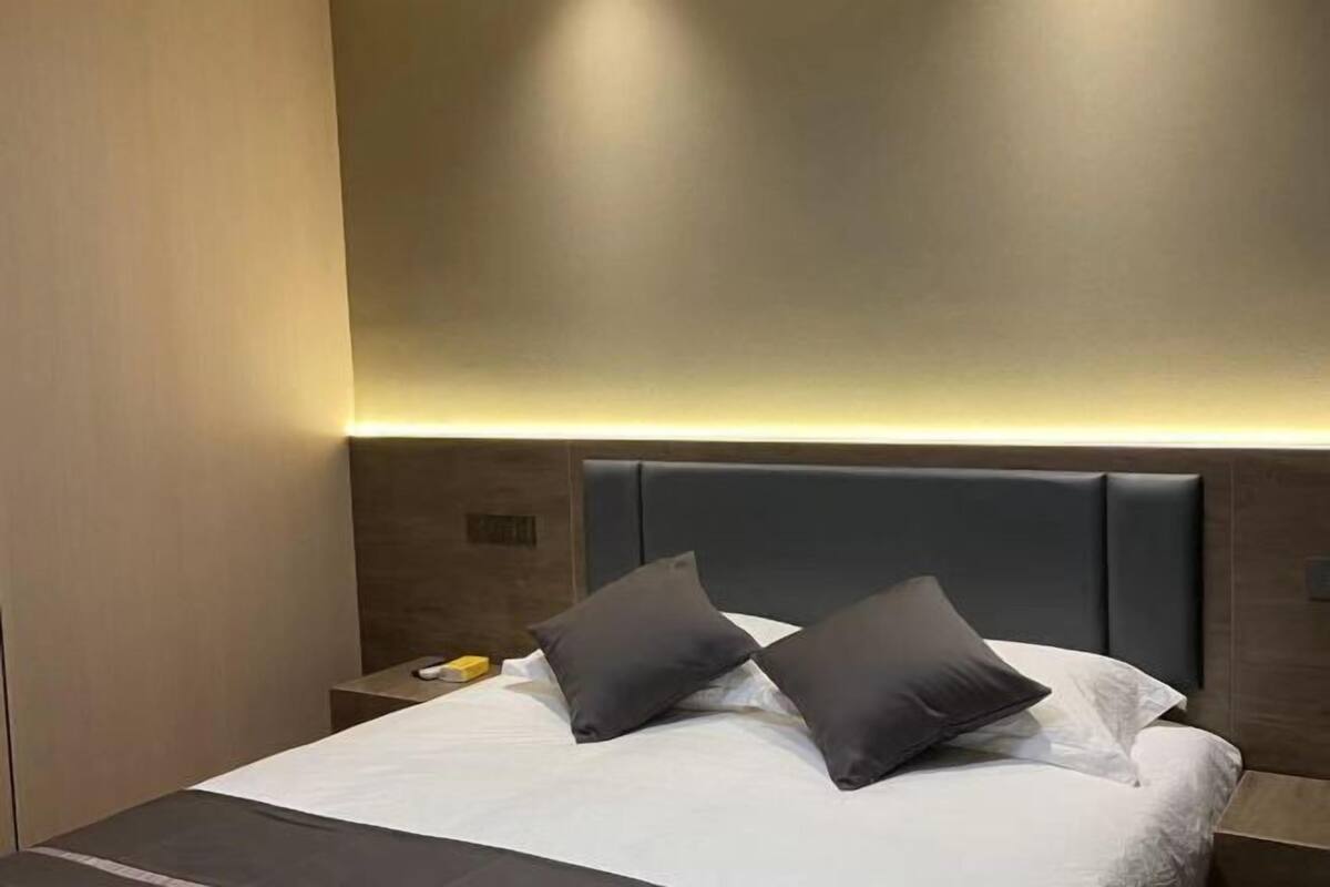 Una habitación de hotel moderna con una cama grande, cabecera oscura y una lámpara de pared.
