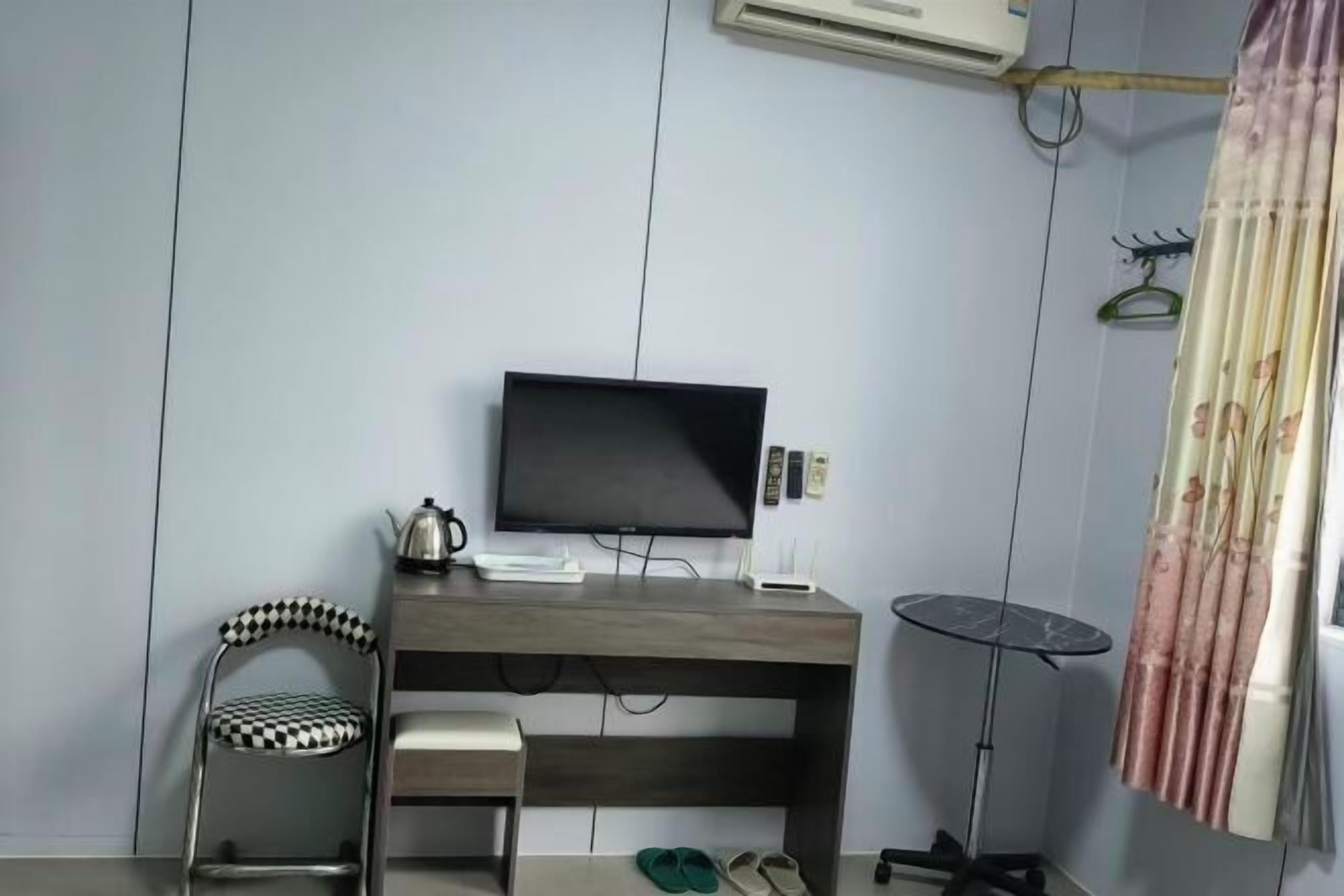 A room with a desk, a chair, a television, a small table, and a pair of slippers.