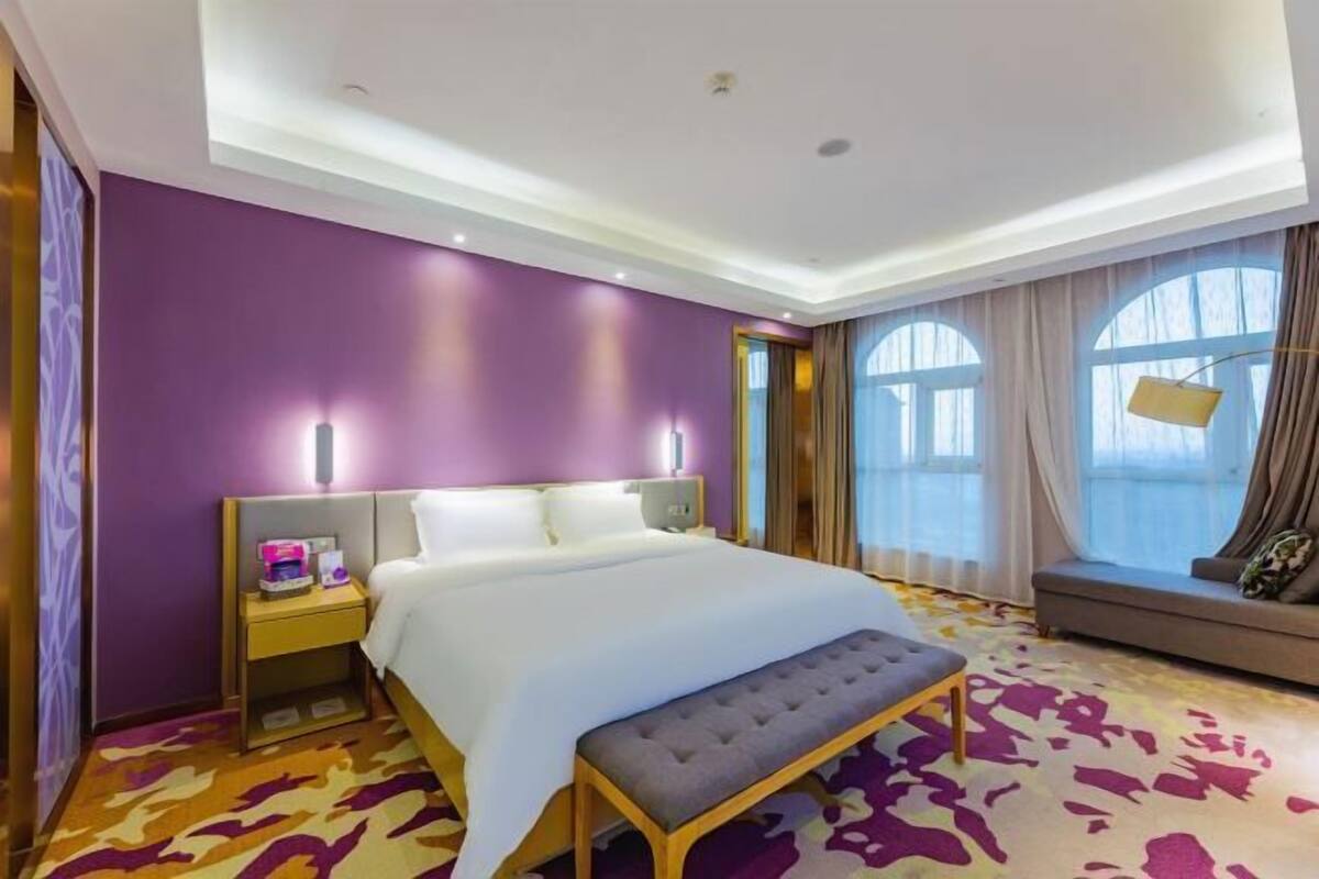 Una habitació d'hotel amb un llit gran, una panxa, una tauleta de nit i una finestra amb cortines.