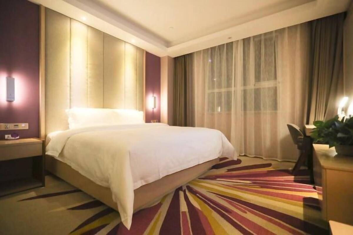 Habitació d'hotel amb un llit gran, una taula de nit, un escriptori amb una cadira i una finestra amb cortines.