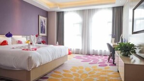 Ein Hotelzimmer mit Bett, Schreibtisch, Stuhl, Pflanze und einem großen Fenster mit Vorhängen.