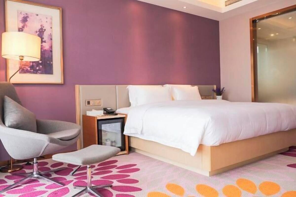 Una habitació d'hotel moderna amb un llit gran, una taula de nit amb una làmpada, una cadira i una taula petita.