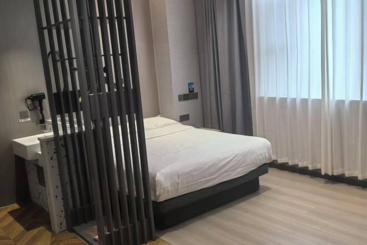 A bedroom with a bed, a desk, a chair, and a window with curtains.