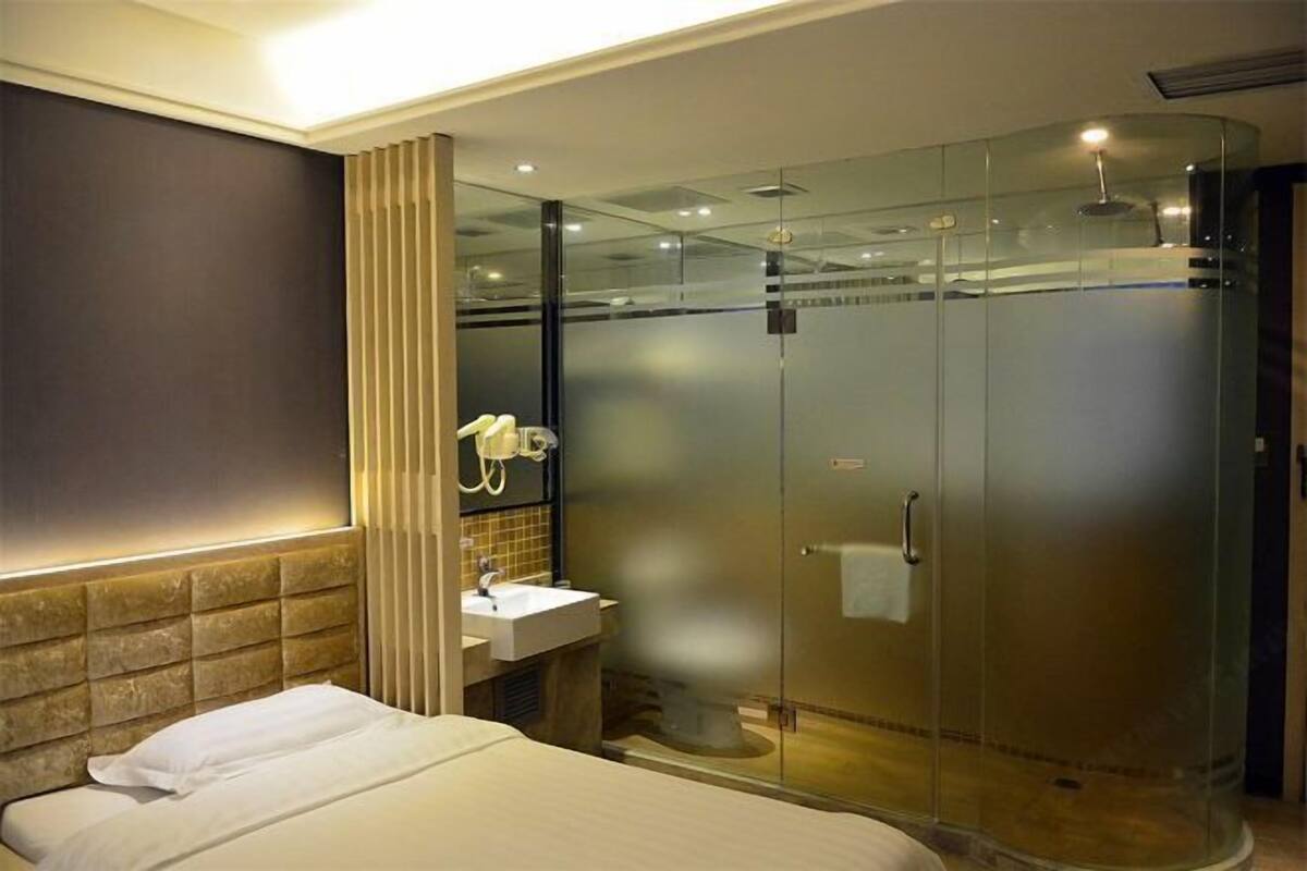 A modern hotel room with a bed, a bathroom with a glass-enclosed shower, and a vanity with a sink.