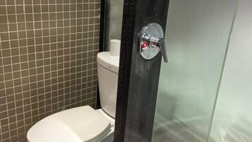 Een badkamer met toilet, douchecabine en betegelde wand.