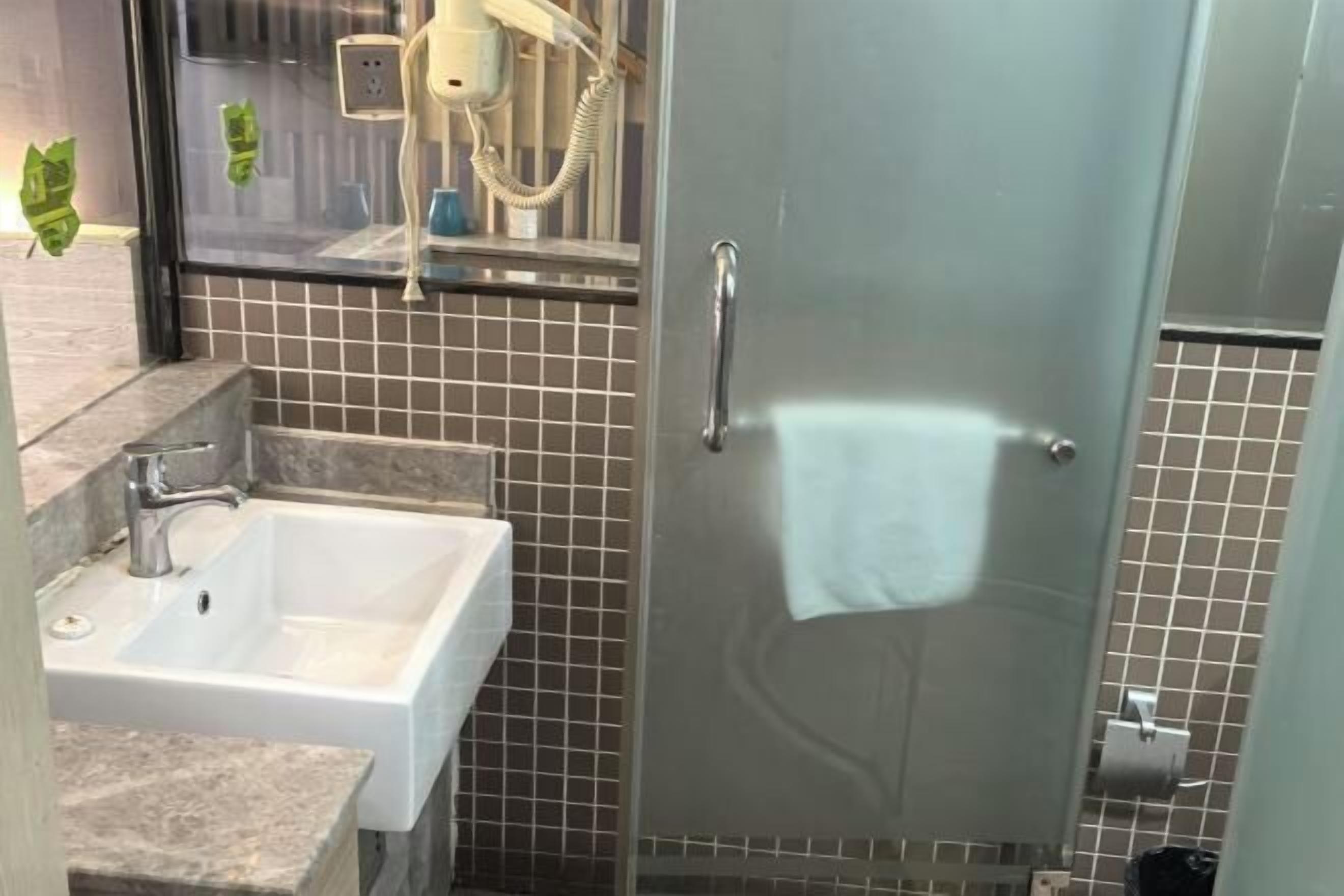 Ein Badezimmer mit einem weißen Waschbecken, einer Duschkabine aus Glas und einem Handtuch, das an der Tür hängt.
