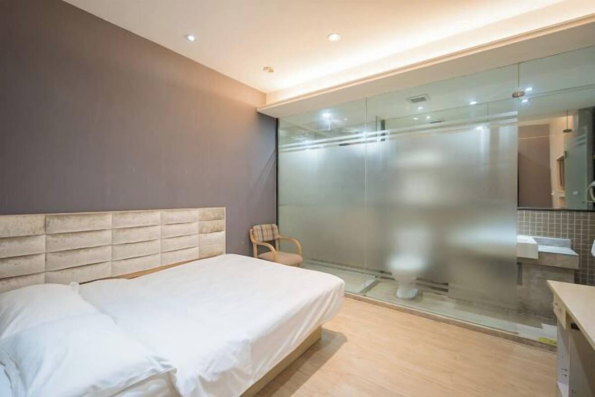 A modern bedroom with a large bed, a chair, and a glass shower enclosure.