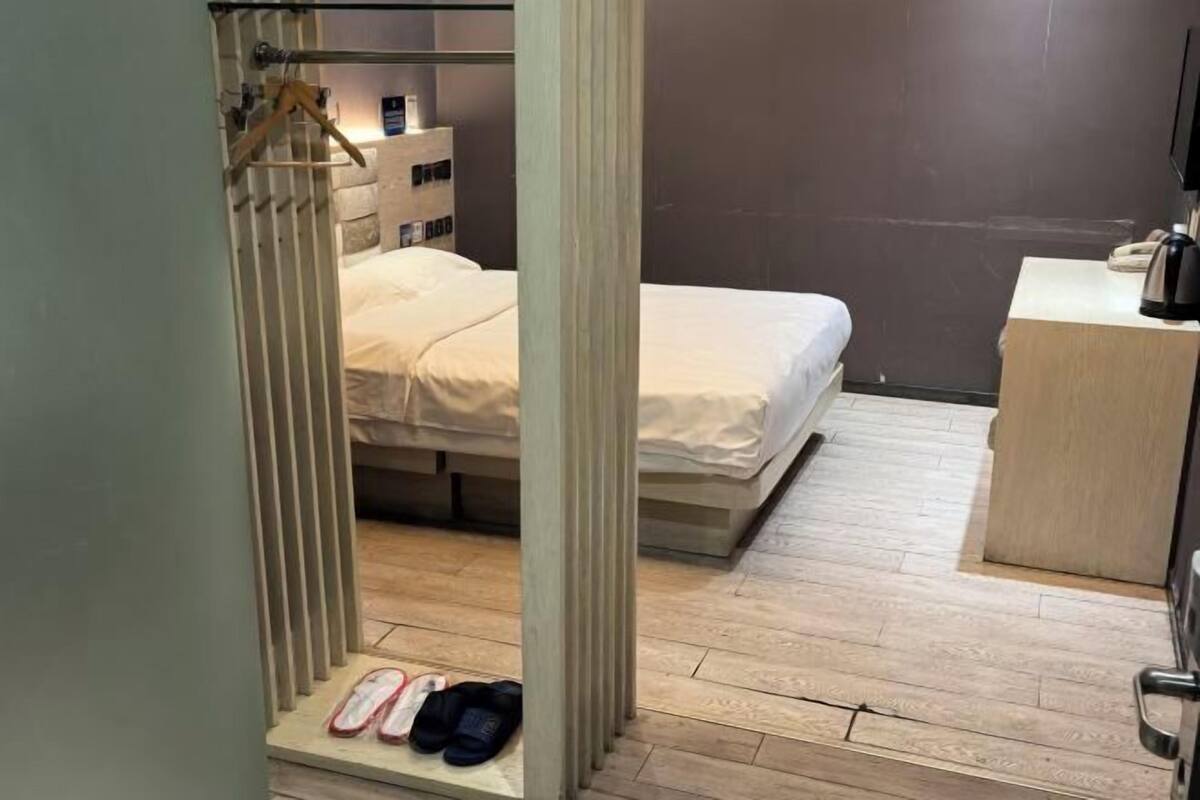 A small, modern hotel room with a bed, a desk, and a wardrobe.
