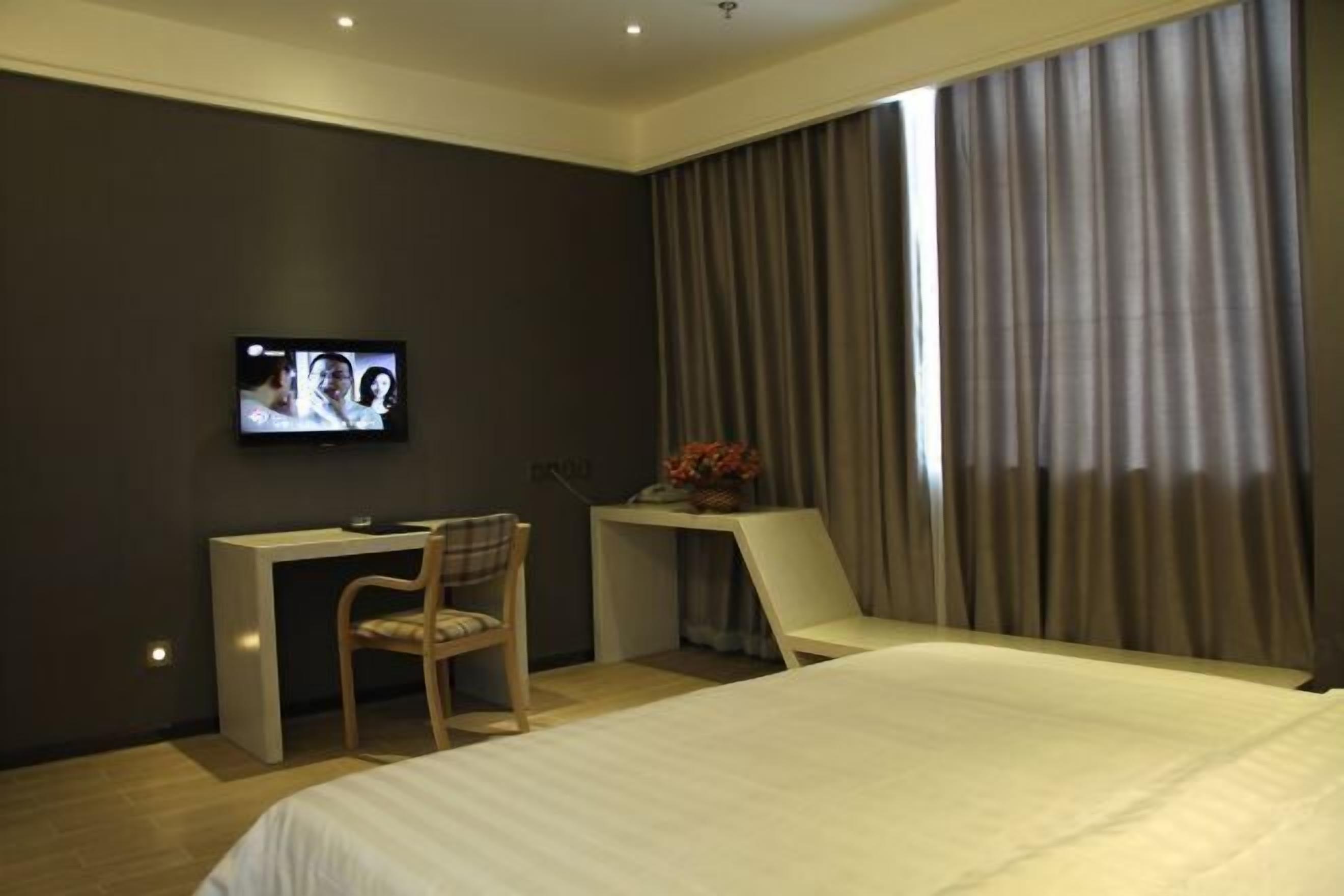 A modern hotel room with a bed, a desk, a chair, a television, and curtains.
