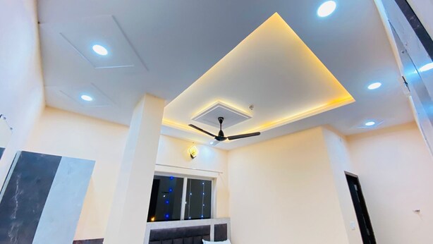 A modern room with a ceiling fan, recessed lighting, and a window with string lights. - Hotel ornate  (Chandauli)