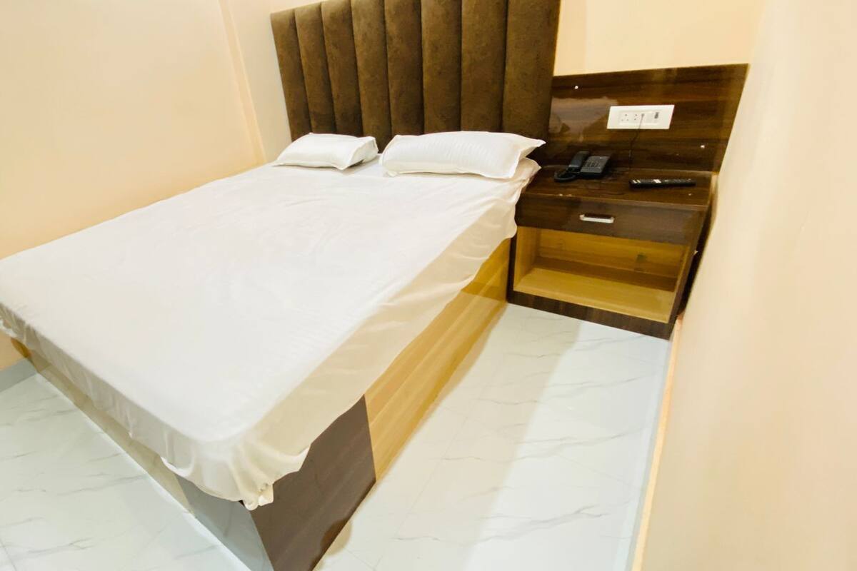 Una cama bien hecha con ropa blanca, un cabecero de madera y una mesita de noche con un teléfono y un control remoto.