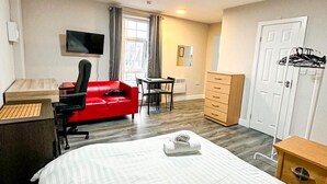 Een hotelkamer met een groot bed, een bureau met een computer, een rode stoel, een aan de muur bevestigde televisie en een kledingkast.