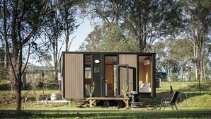 A small, modern cabin with a sliding door, a bed, and a table. - The Mini Chalet by Tiny Away (Mundoolun)