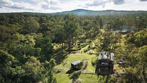 An aerial view of a rural property with a small building, a fenced area, and a path leading to a larger structure in the background. - The Mini Chalet by Tiny Away (Mundoolun)