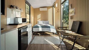 A modern bedroom with a bed, bedside table, and a desk with a chair. There is a window providing natural light and a view of greenery outside. - The Mini Chalet by Tiny Away (Mundoolun)