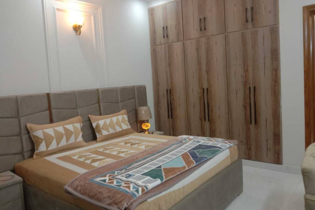 A bedroom with a bed, nightstands, a wooden wardrobe, and a wall-mounted light.