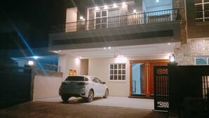 A two-story house with a car parked in the driveway, a balcony on the upper floor, and a gated entrance. - SKM Lodges (Islamabad)