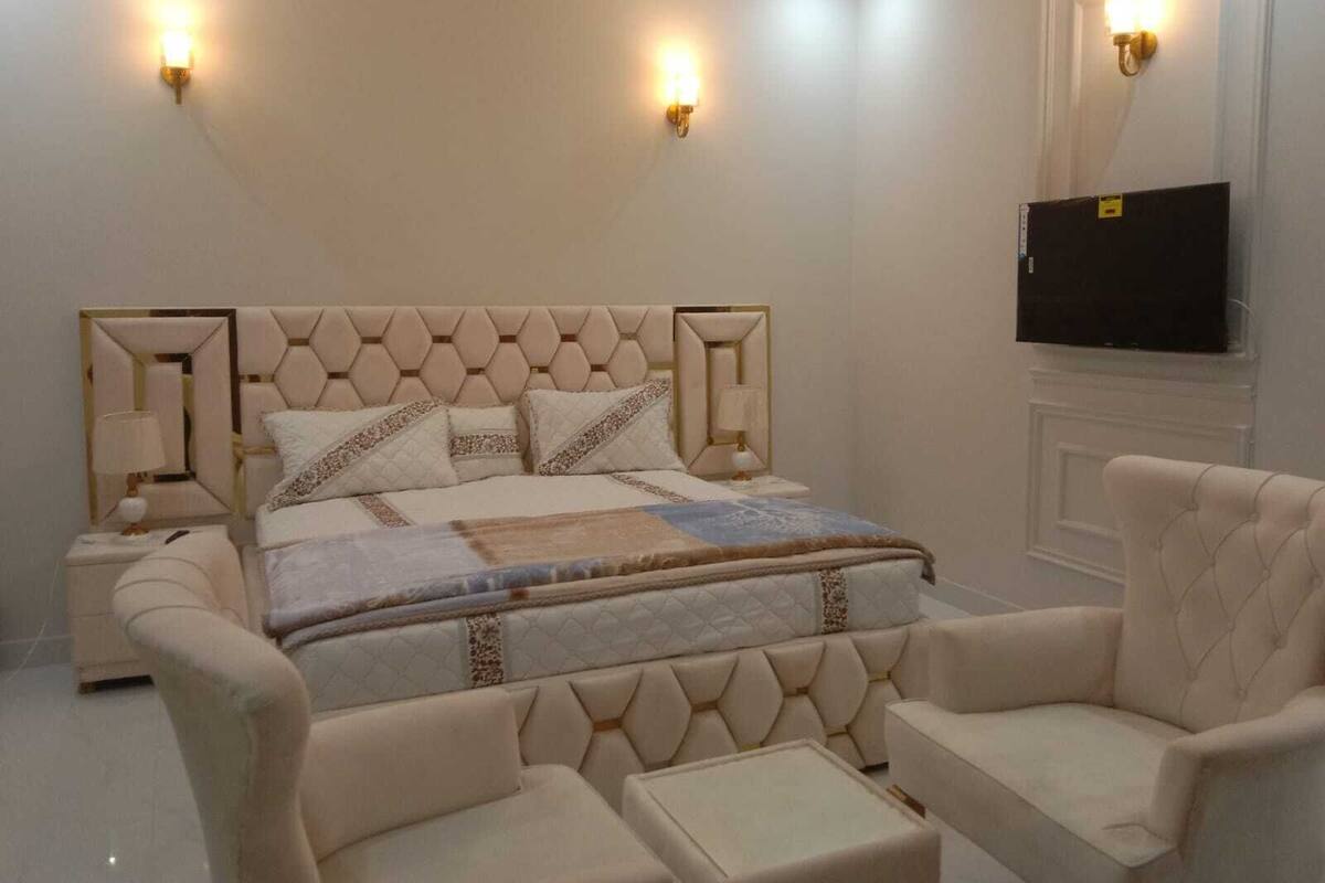 A bedroom with a large bed, two bedside tables, two lamps, a television, and two armchairs.