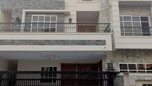 A modern two-story house with a stone facade, a gated entrance, and a balcony on the upper floor. - SKM Lodges (Islamabad)