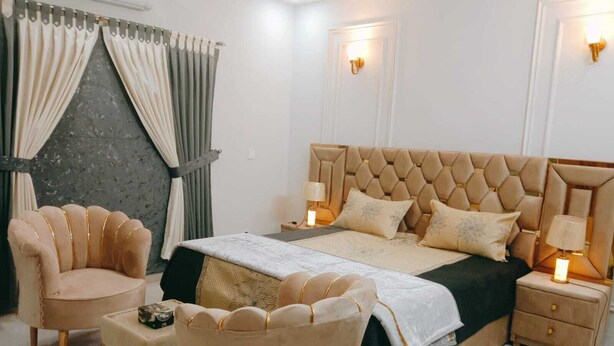 A bedroom with a large bed, two nightstands, a chair, and a small table. - SKM Lodges (Islamabad)