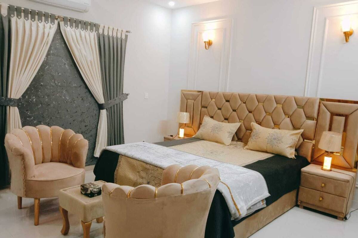 A bedroom with a large bed, two nightstands, a chair, and a small table.