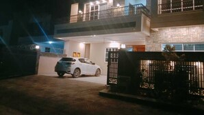 A two-story house with a balcony, a car parked in the driveway, and a gated entrance. - SKM Lodges (Islamabad)