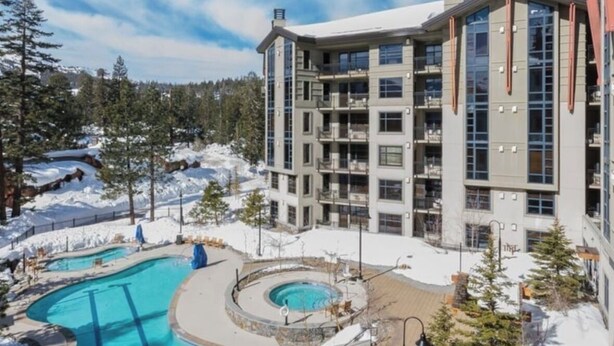 Un hotel de varios pisos con zona de piscina, rodeado de paisaje nevado y árboles.