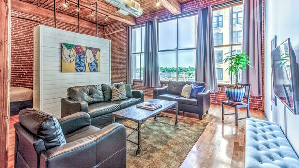 A modern living room with leather sofas, a coffee table, and a large window with curtains. - Washington Ave Loft + Sleeps 8 + 24/7 Security (St. Louis)