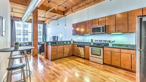 A modern kitchen with wooden cabinets, stainless steel appliances, and a bar area with stools. - Washington Ave Loft + Sleeps 8 + 24/7 Security (St. Louis)