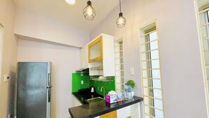 Una cocina compacta con refrigerador, una encimera negra y una ventana con persianas.