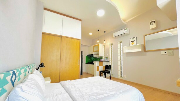 Un dormitorio con cama, armario, kitchenette y baño con espejo y retrete.