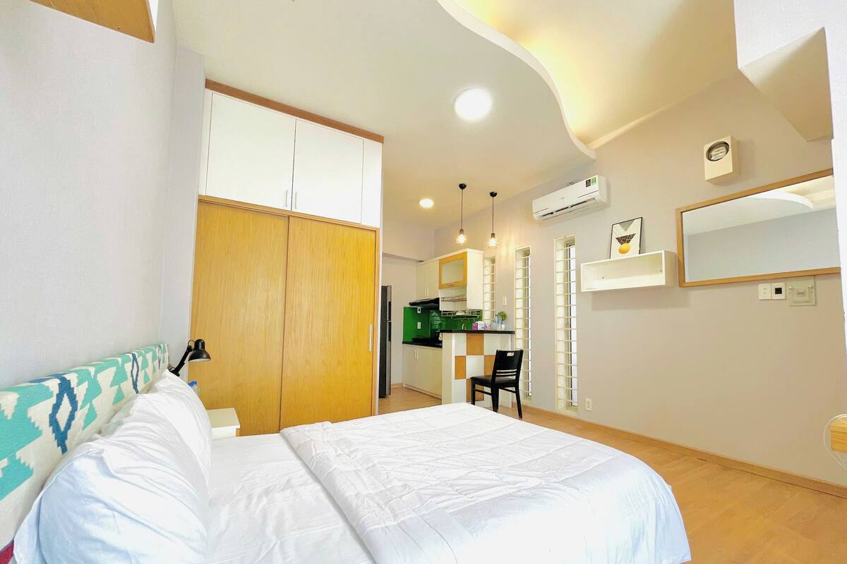 A bedroom with a bed, wardrobe, kitchenette, and a bathroom with a mirror and toilet.