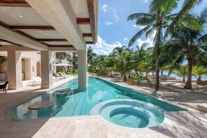 Une piscine avec un jacuzzi, entourée de palmiers et de chaises longues, offrant une vue sur l’océan.