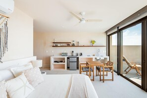 Une chambre d’hôtel moderne équipée d’un lit, d’un bureau, d’une kitchenette et d’un balcon avec une chaise.