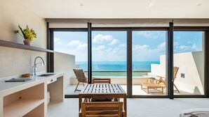 Una cocina moderna con una mesa y sillas de madera, una planta en maceta y vistas al océano a través de amplios ventanales correderas.