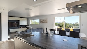 Een moderne keuken met een centraal kookeiland, een eetgedeelte met uitzicht en een groot raam.