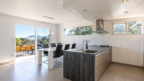Een moderne keuken met een ruim eiland, een eetgedeelte met uitzicht en een balkon met buitenmeubilair.