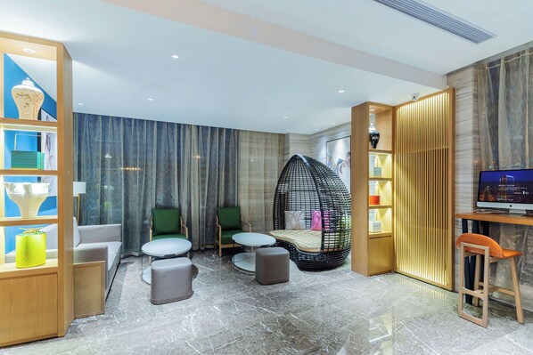 A modern hotel room with a seating area featuring a green chair, a hanging egg chair, and a small round table. There is a wooden bookshelf with decorative items and a television on a wooden stand. - LIZ International Hotel Guangzhou Olympic Sports Center International Financial City Branch - Free Shuttle Bus to Canton Fair Complex During Canton Fair Period (Guangzhou)