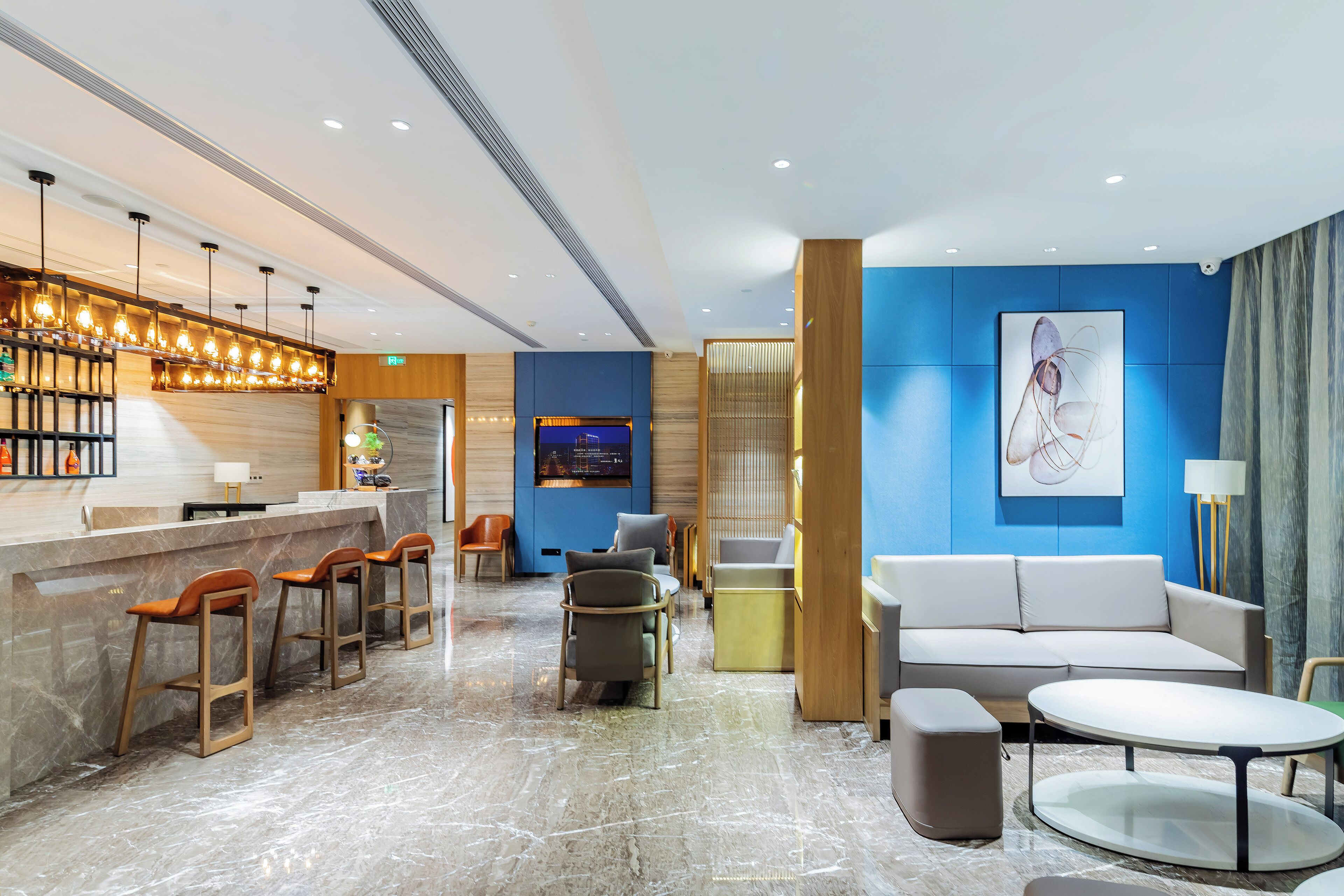 A modern lobby with a marble floor, a reception desk, bar stools, seating area, and a large abstract painting on the wall.