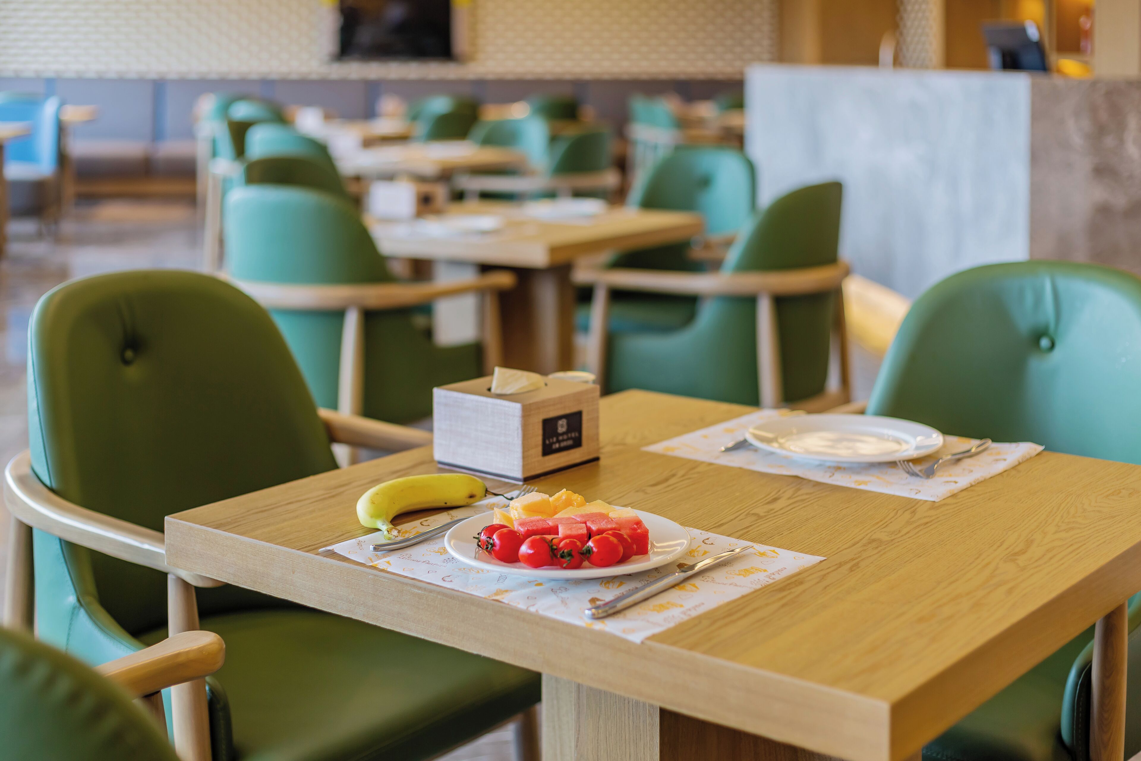 A dining area with green chairs and tables, a plate of fruit, and a box of tissues.
