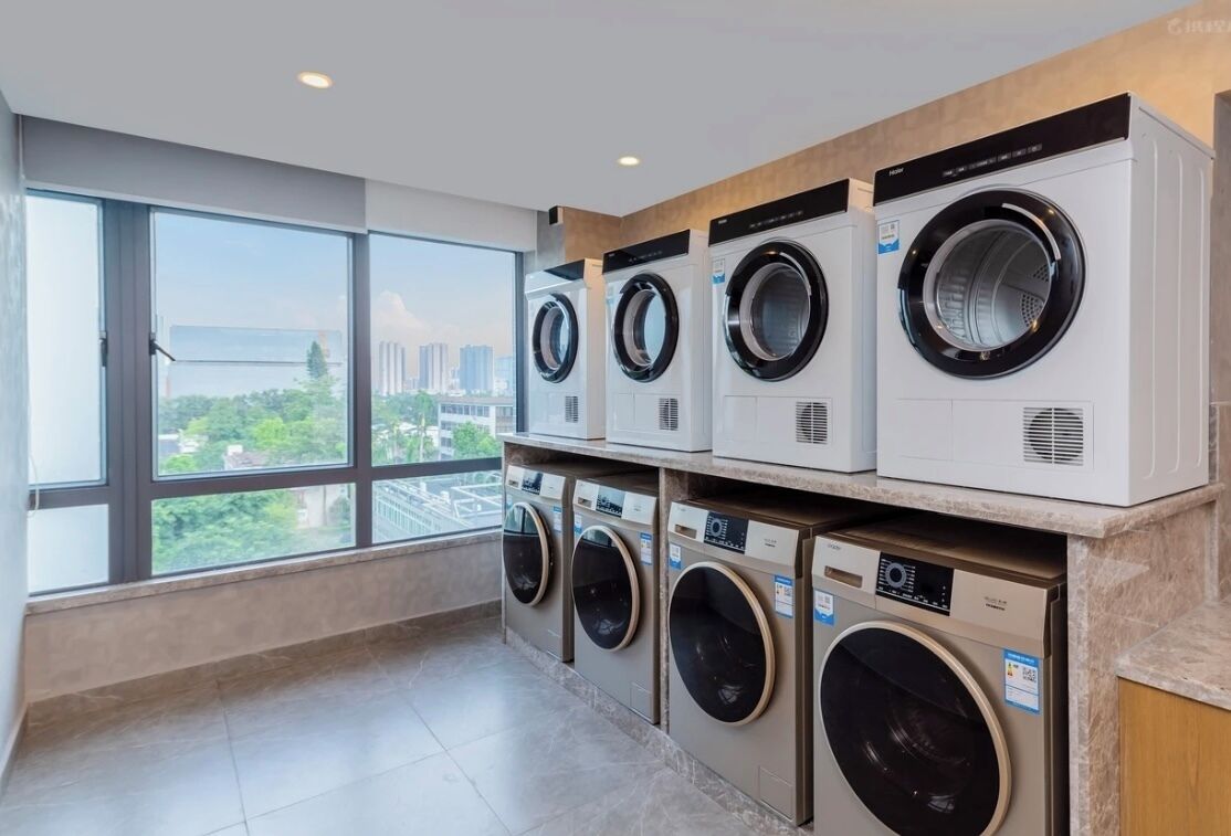 A laundry room with multiple washing machines, large windows, and a view of a cityscape.
