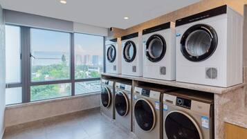 A laundry room with multiple washing machines, large windows, and a view of a cityscape.