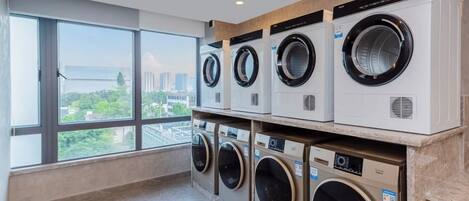 Un lavadero con varias lavadoras, amplias ventanas y vistas a un paisaje urbano.