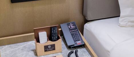 Une chambre d’hôtel avec un lit, une table de chevet avec une télécommande, un téléphone et un bloc-notes.