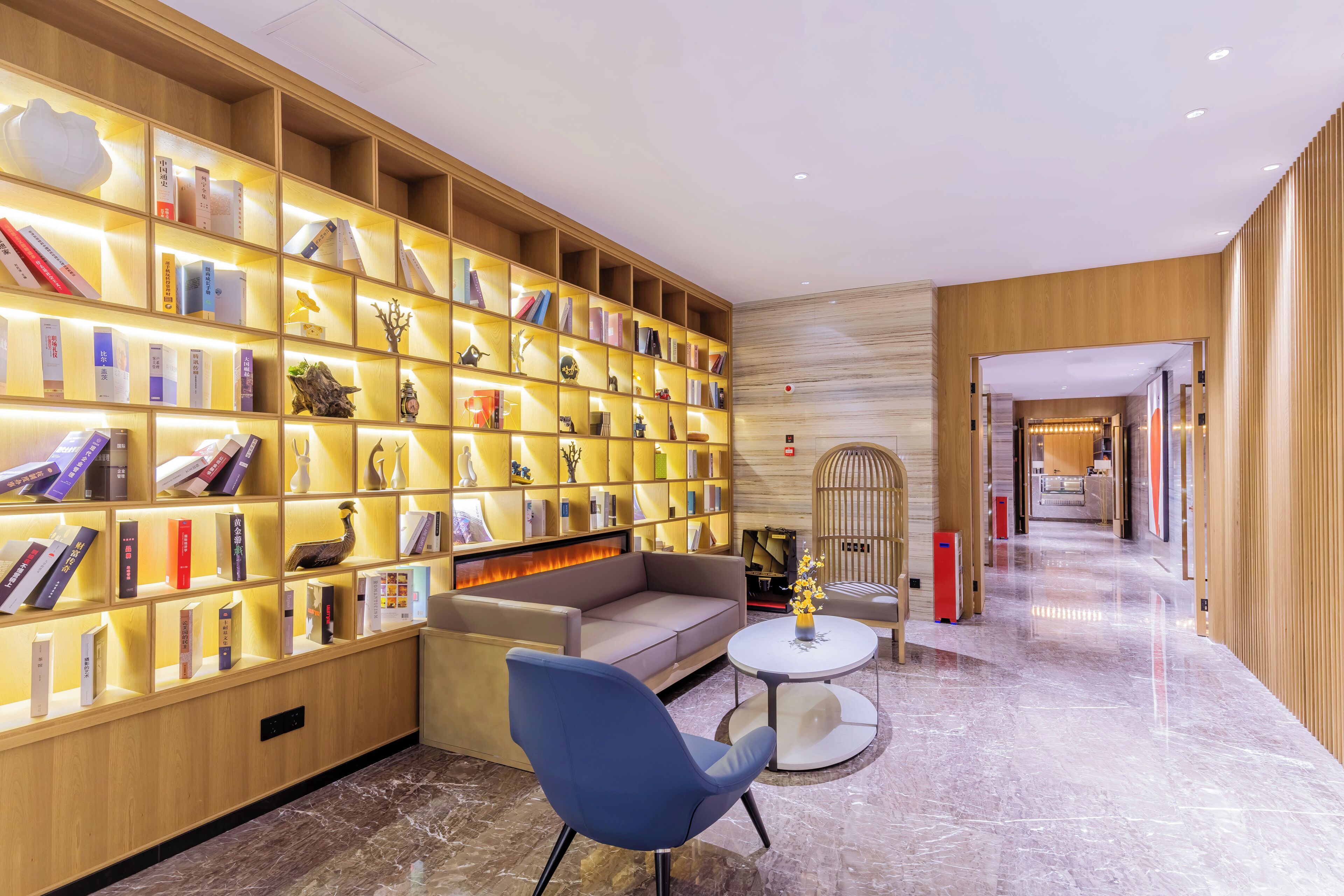 Een moderne hotel lobby met een grote boekenkast, een bank, een ronde tafel en een decoratieve vogelkooi.